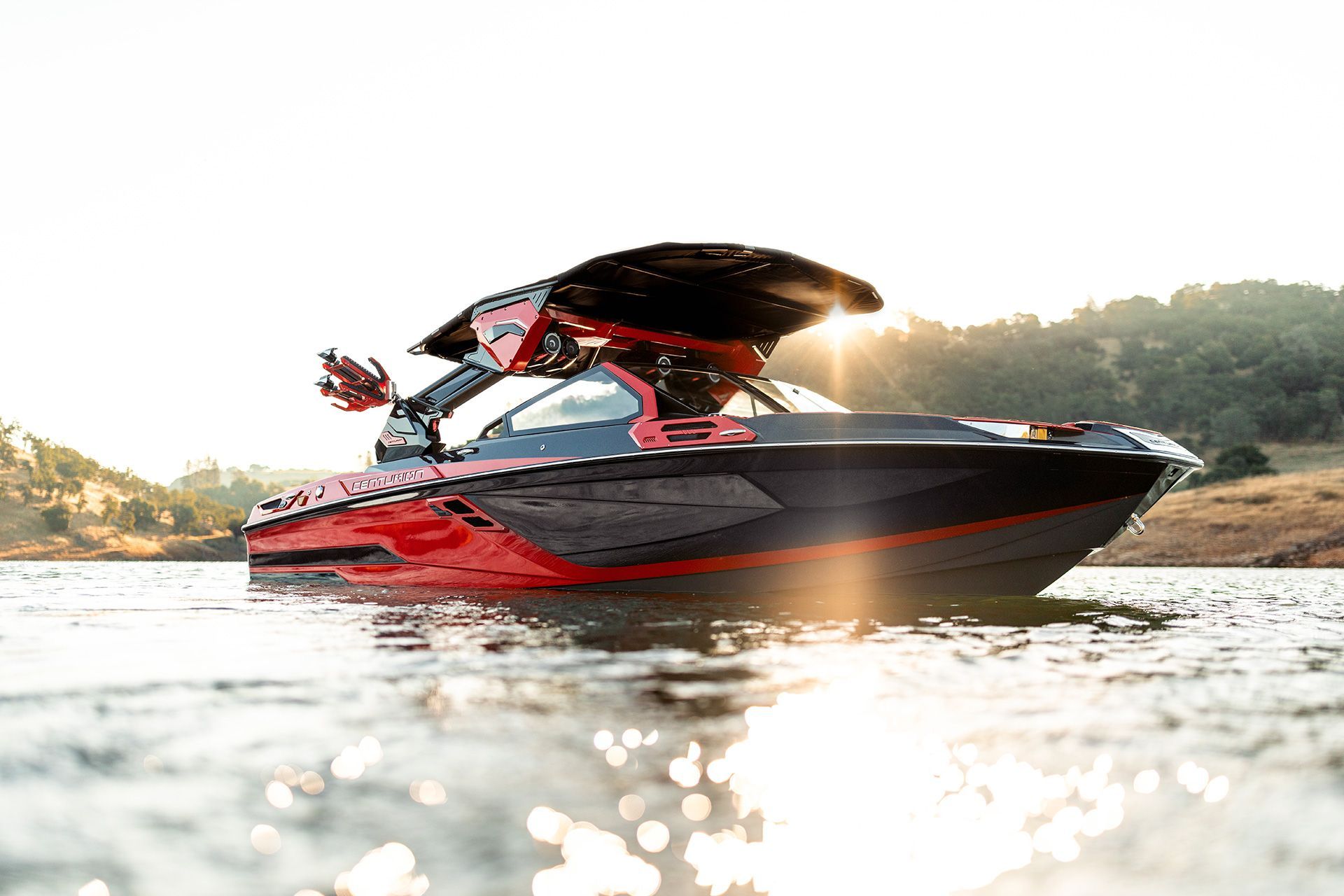 Red and black motorboat on calm water, with a black tower against a bright sky.
