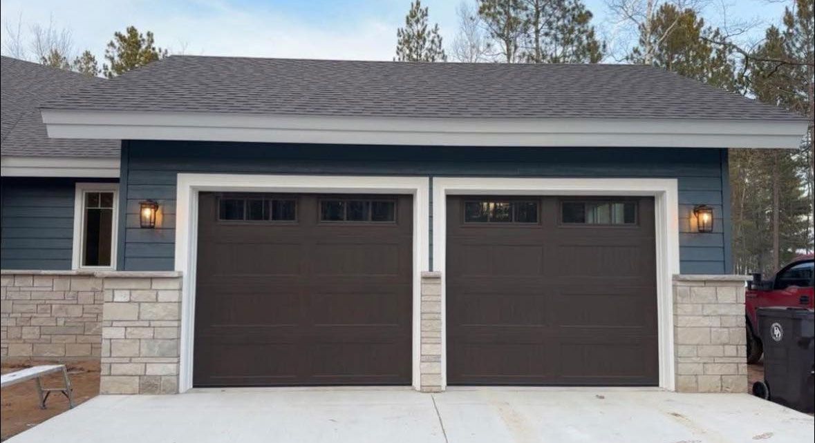 A blue house with two brown garage doors and a red truck parked in front of it.