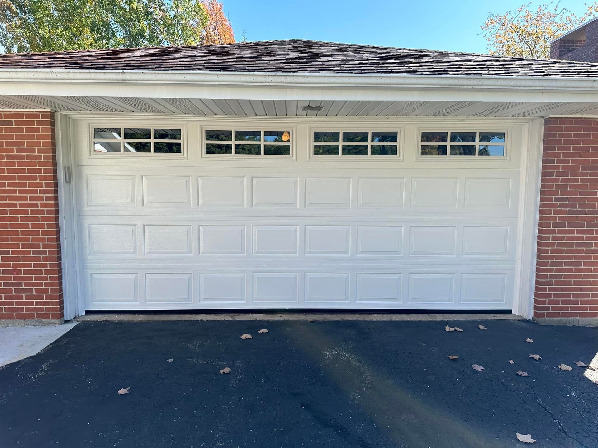 A white garage door is sitting in front of a brick house.