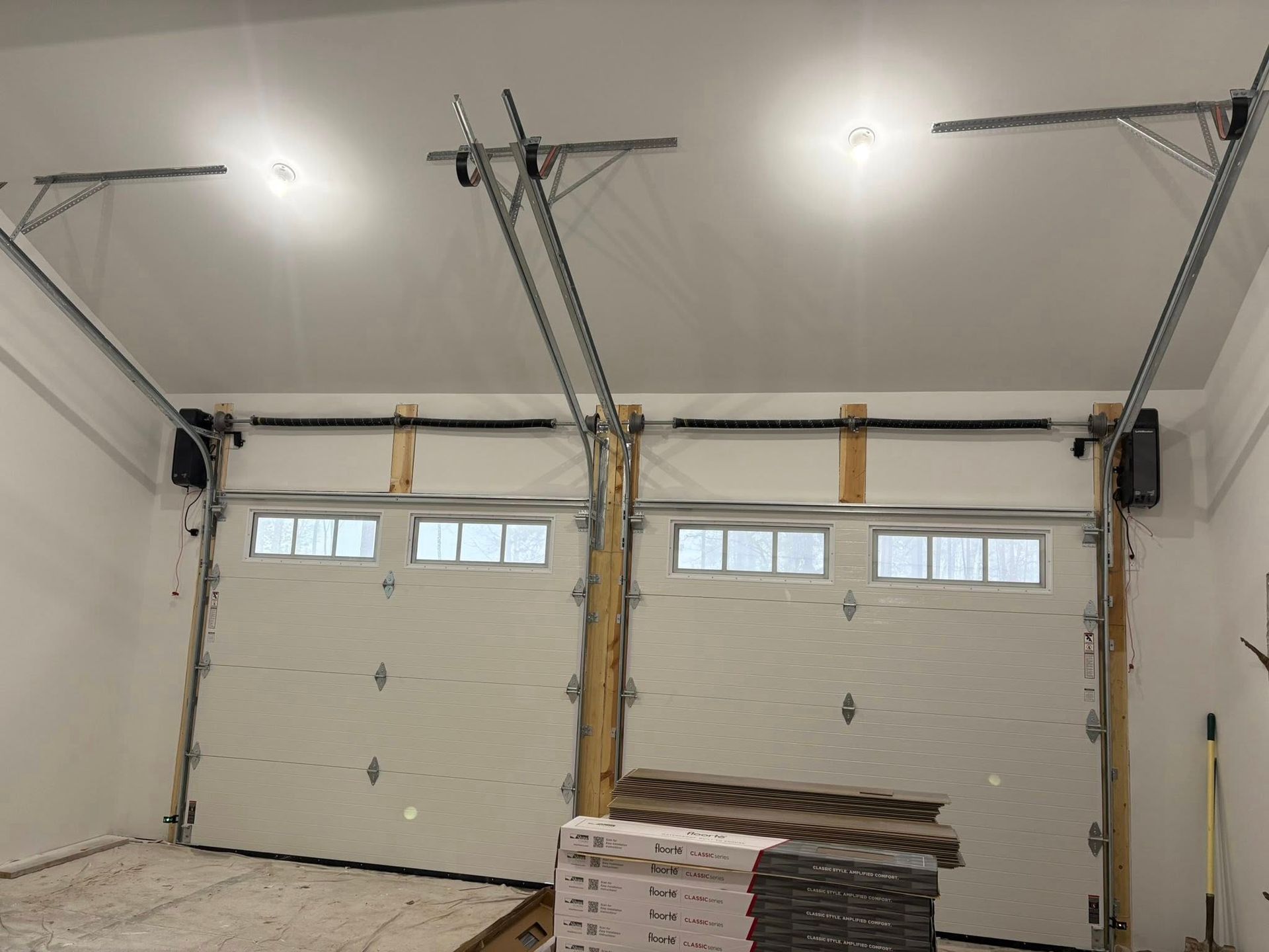 A garage with two garage doors open and a stack of wood in the corner.