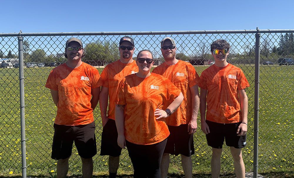 A group of people wearing orange shirts are standing in front of a chain link fence.