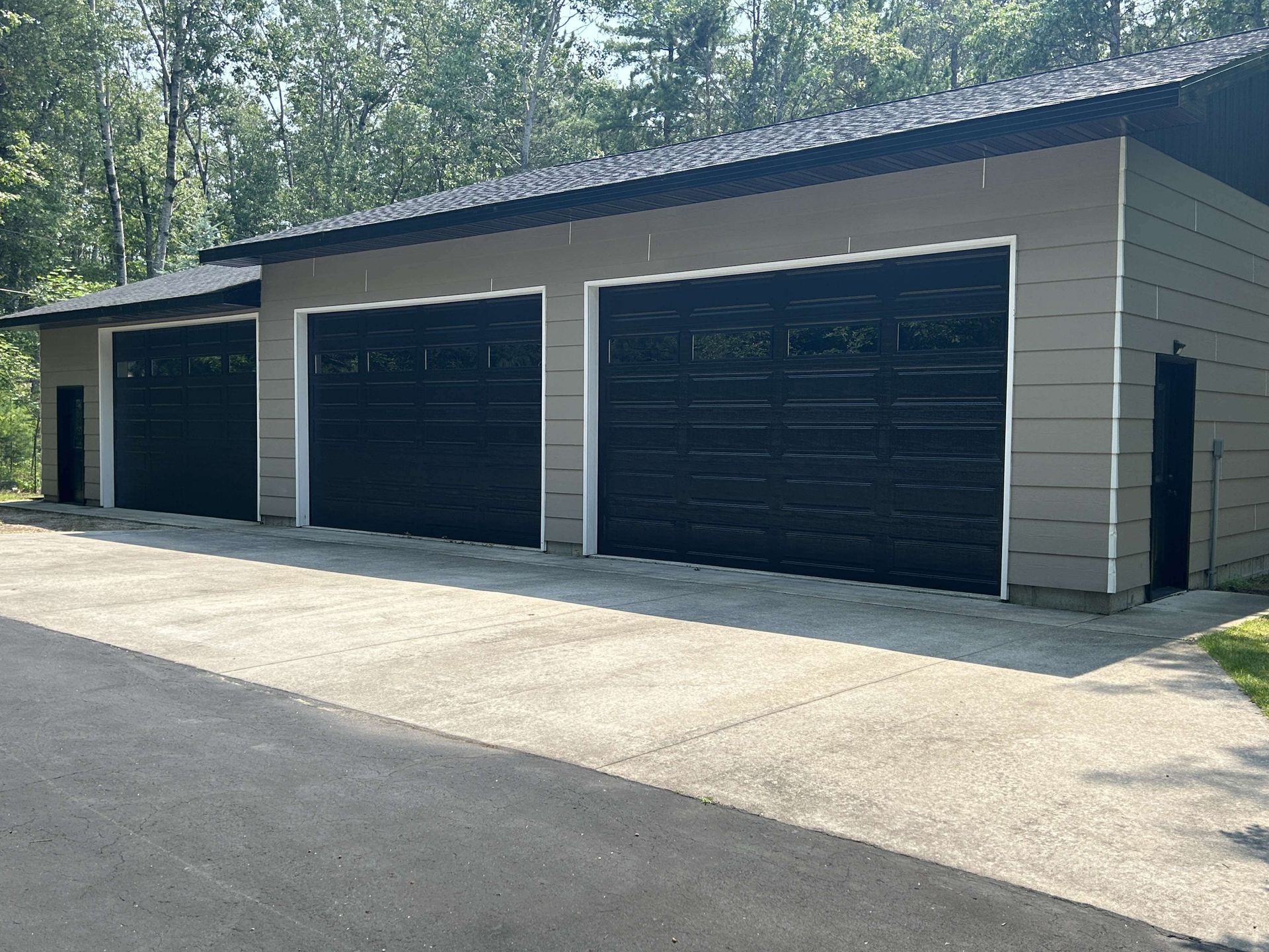A garage with three black garage doors on a sunny day.
