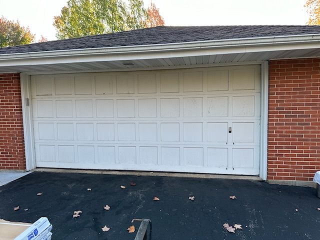 A white garage door is sitting in front of a brick house.