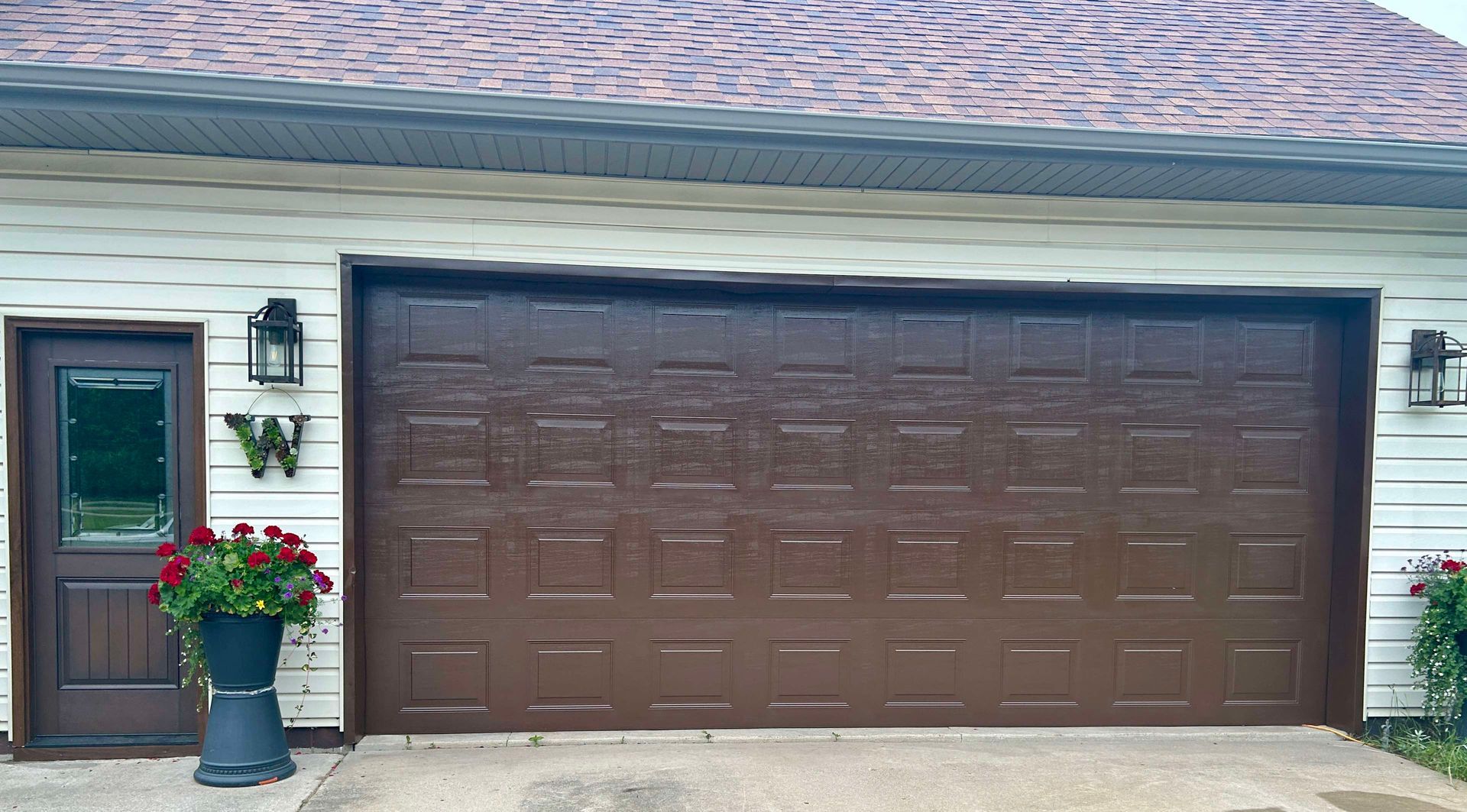 A white house with a brown garage door and a door with the letter w on it