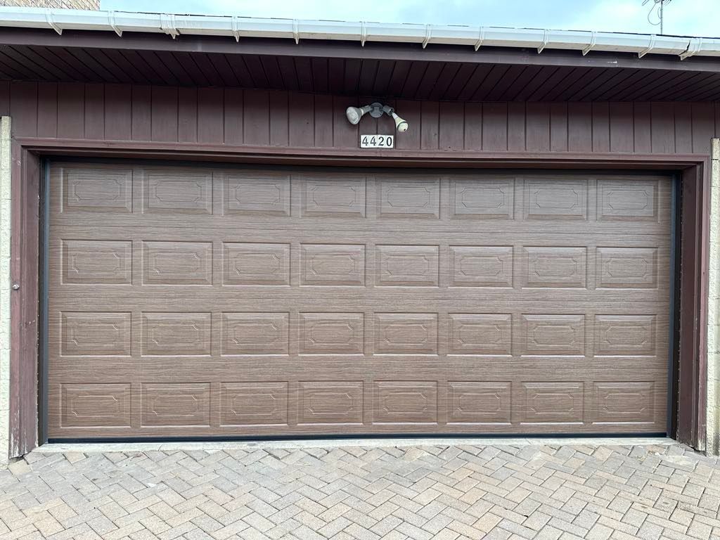A brown garage door is sitting on a brick driveway.