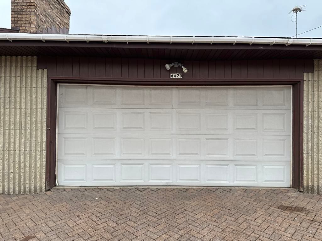 A white garage door with a brown trim is sitting on a brick driveway.