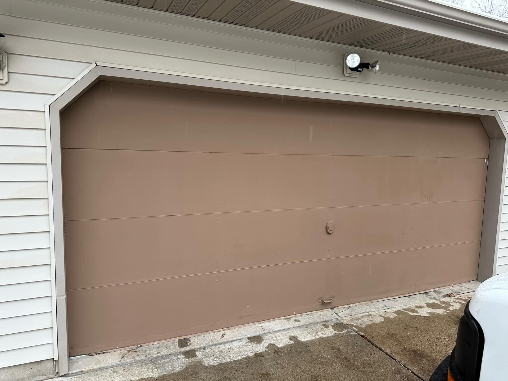 A brown garage door is sitting next to a white house.