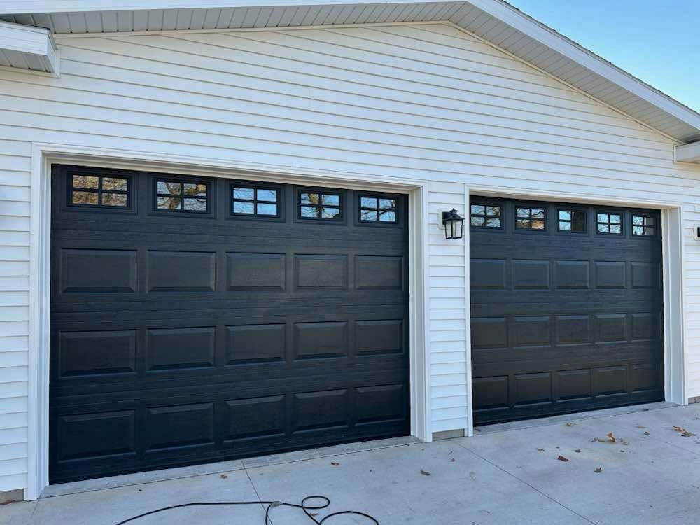 Two black garage doors are on a white house.