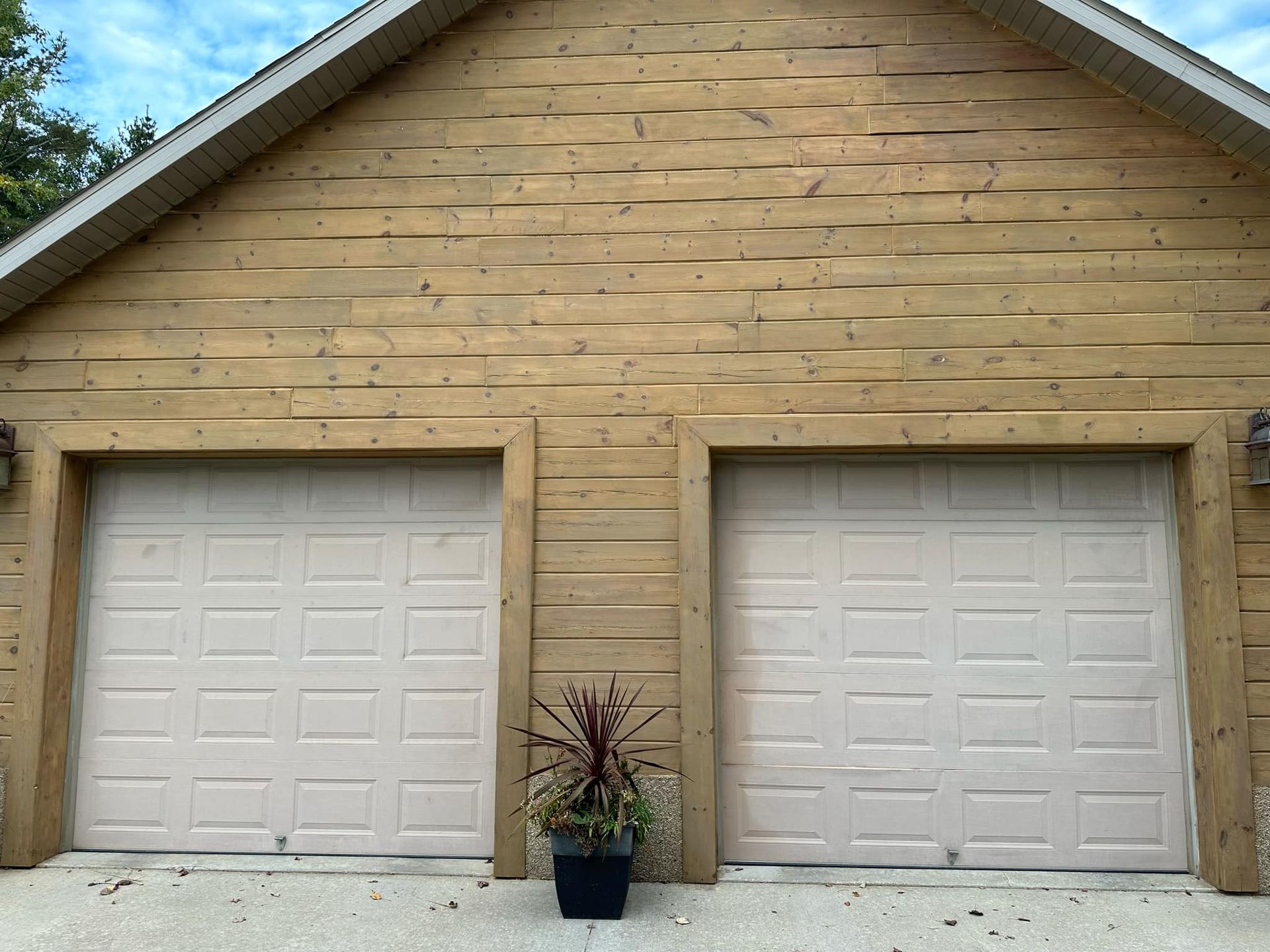 A garage with two white garage doors and a potted plant in front of it.
