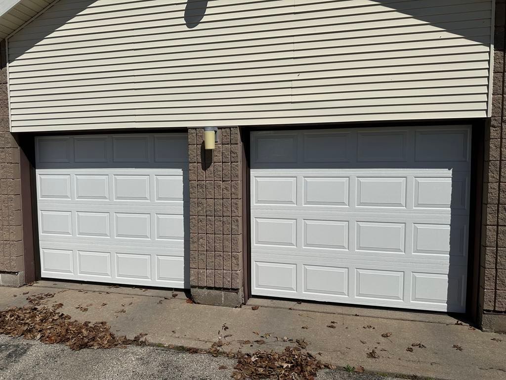 A pair of white garage doors on the side of a house.