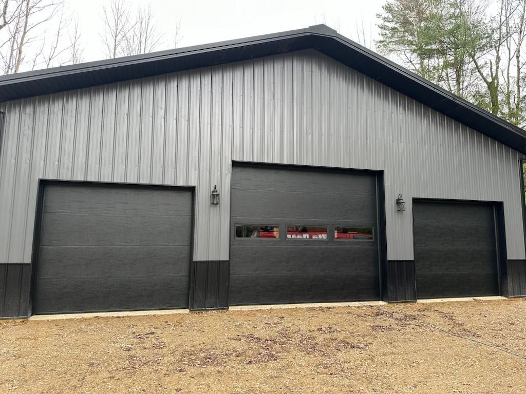 A garage with three black garage doors is sitting on top of a dirt hill.