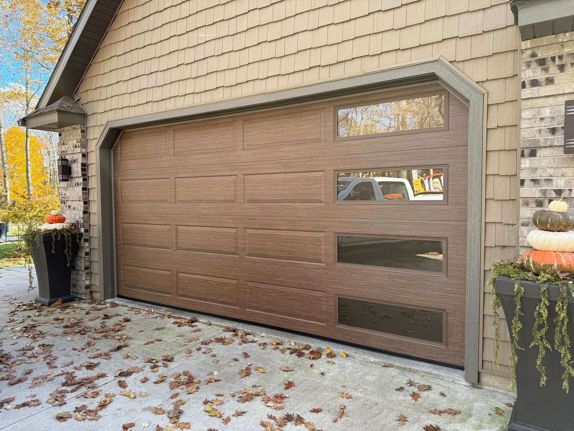 Brown garage door with three glass panels, tan siding, and decorative planters.