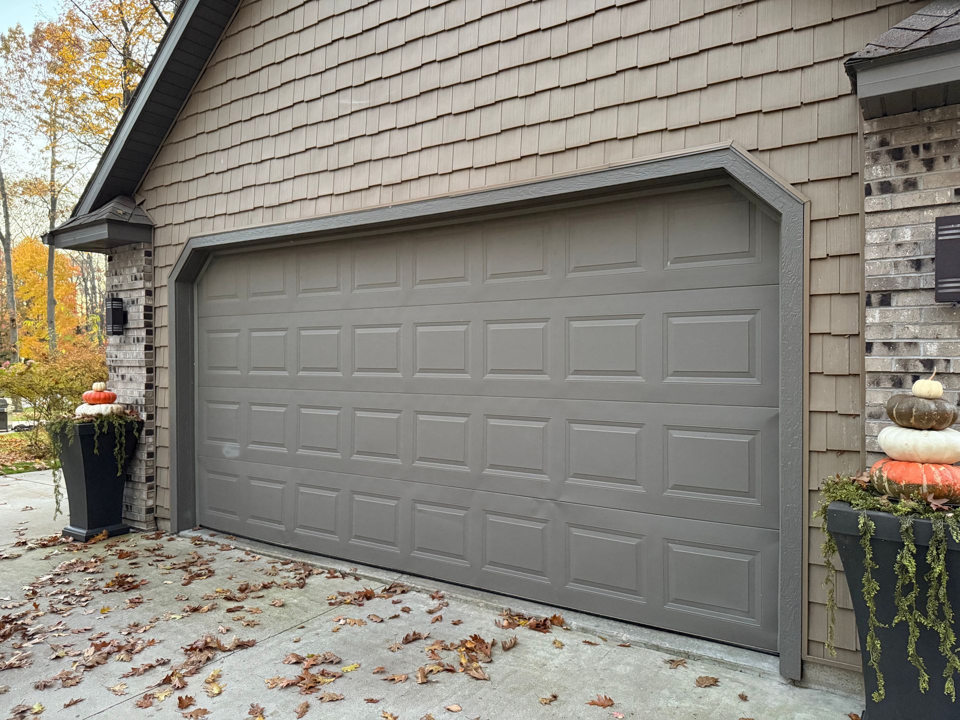 Gray garage door on a house with brown shake siding, surrounded by fall foliage.