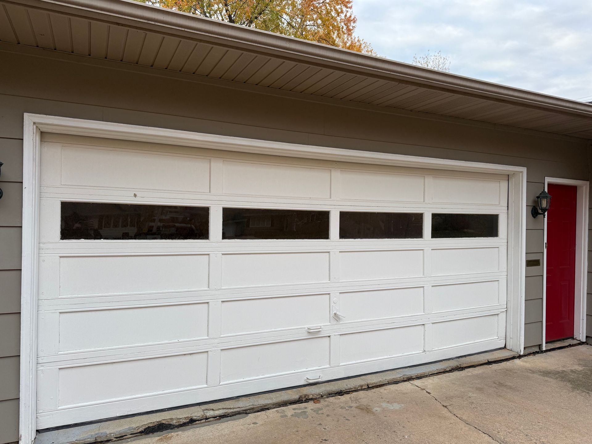 White garage door with rectangular windows, adjacent to a red door and a brown exterior wall.