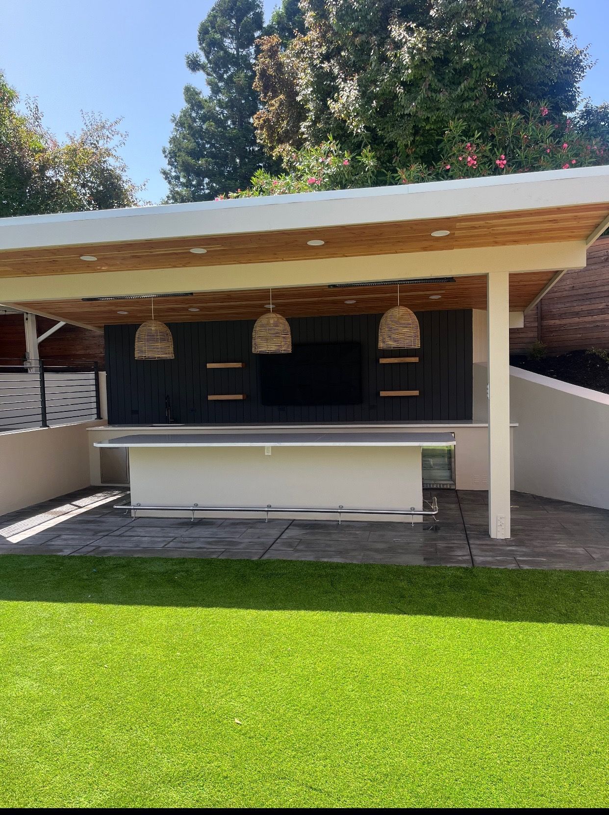 Outdoor backyard bar with white roof, hanging lights, and a counter over bright green grass
