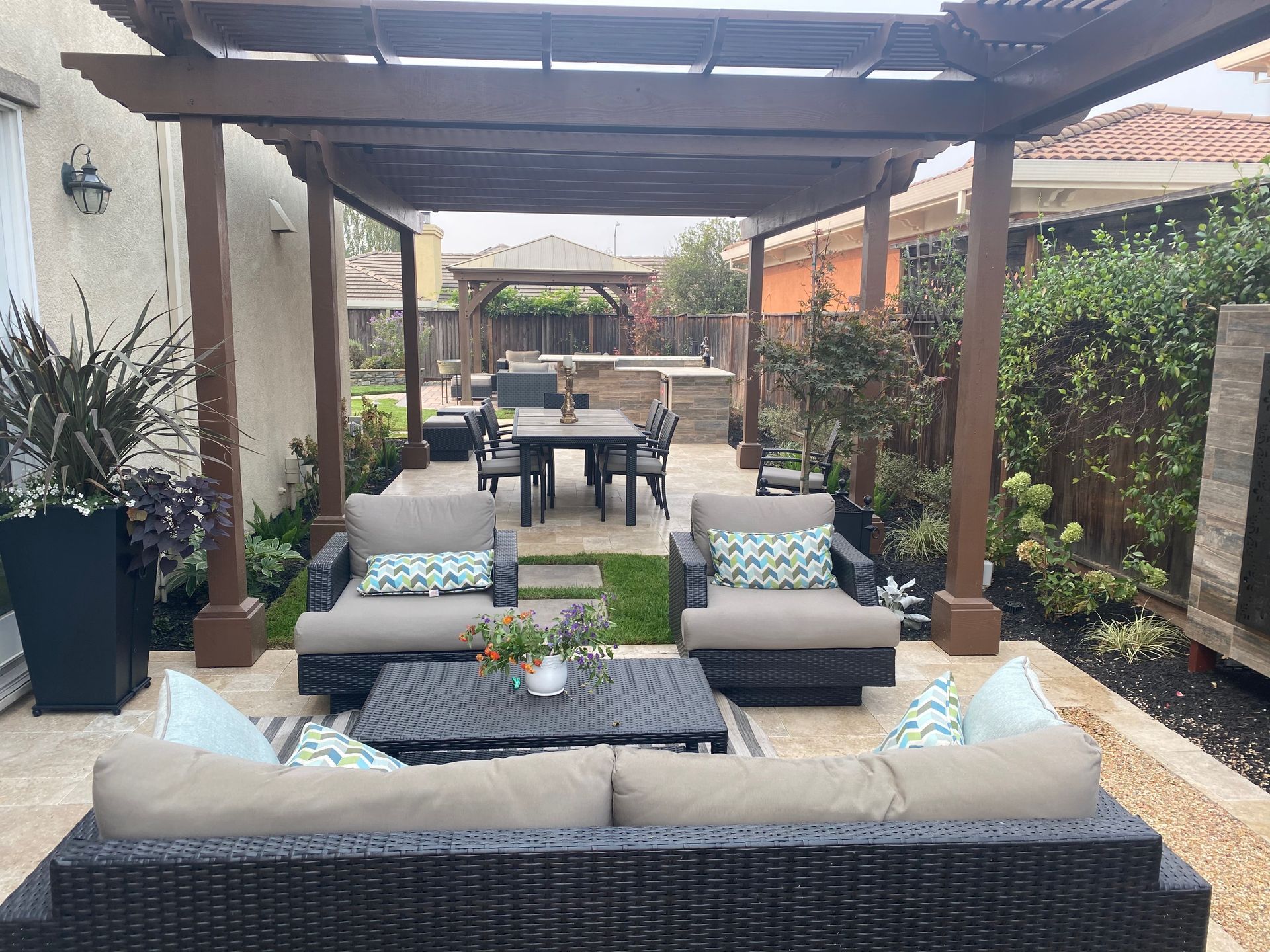 Covered patio lounge with gray sofas, blue pillows, coffee table, and dining area beyond