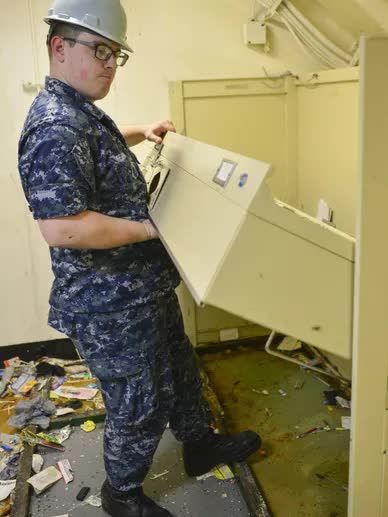 Man in navy uniform with hard hat, removing cabinet in a messy room.