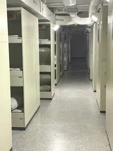 Narrow hallway lined with white cabinets and fluorescent lighting, leading to a dark, unseen area.