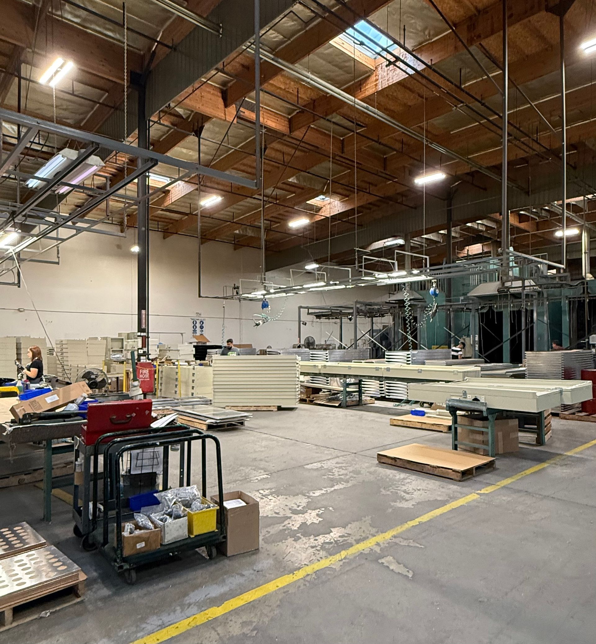 Warehouse interior with machinery, pallets, and a cart on a concrete floor under a high ceiling.