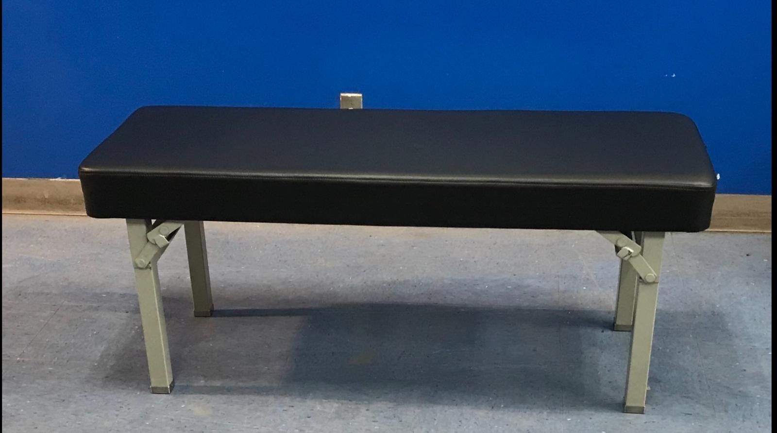 Black padded bench with folding metal legs against a blue wall.