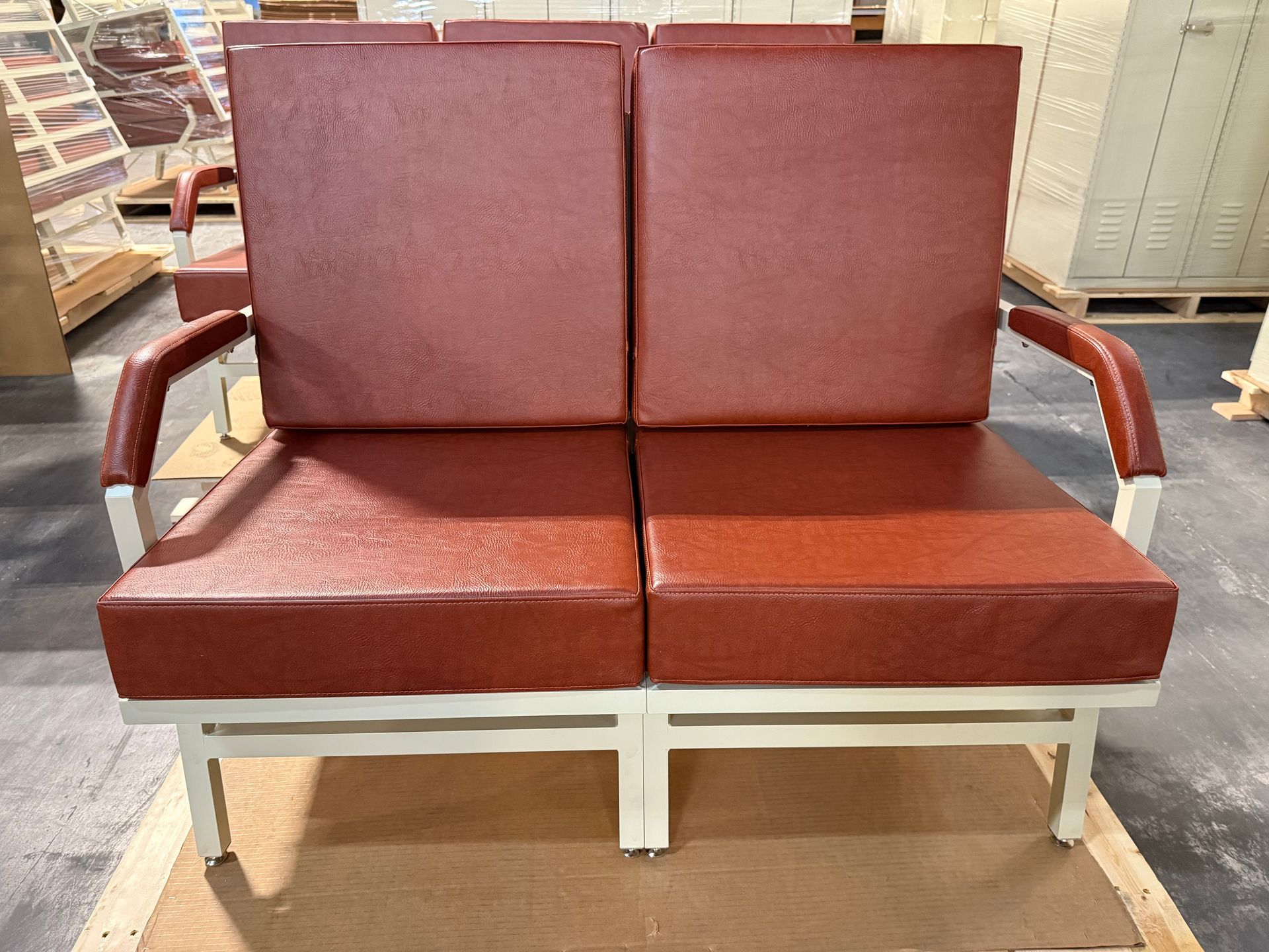 Two-seat red vinyl sofa with white metal frame, in an industrial setting.