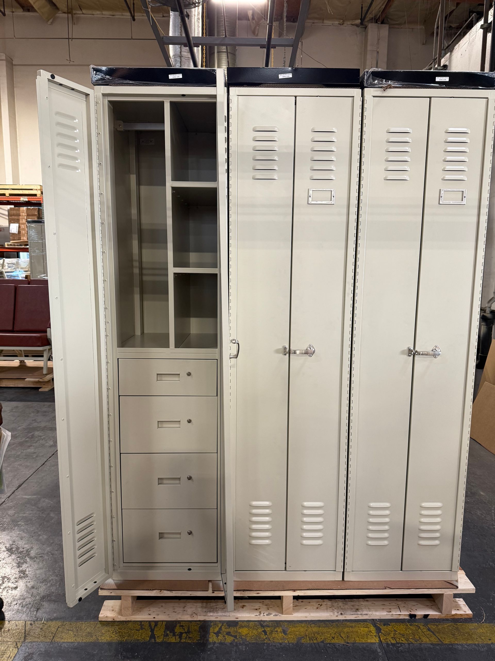 Three beige metal lockers, one open showing shelves and drawers, on a pallet in a warehouse.