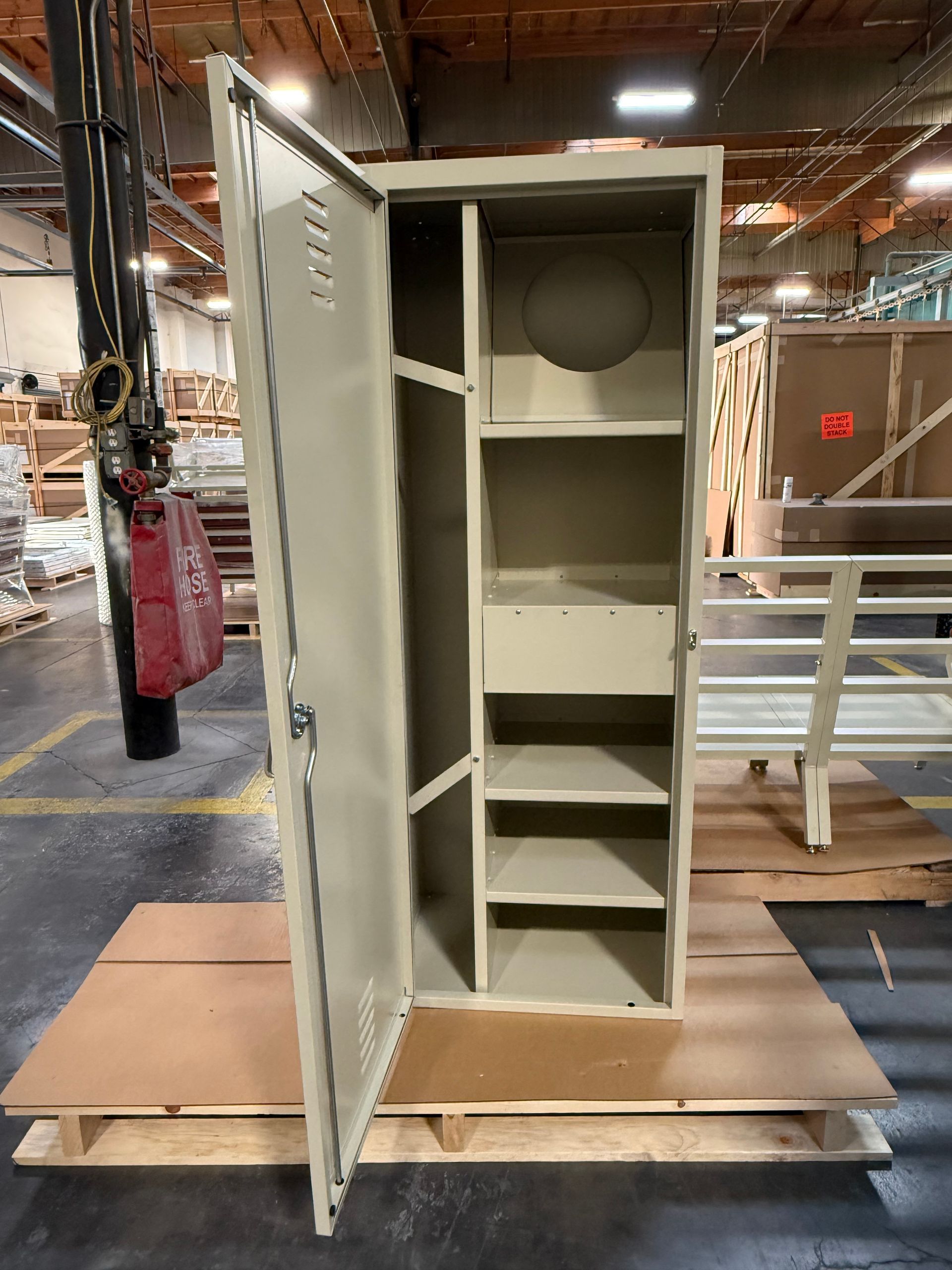 Beige metal storage cabinet, open, with shelves, in a factory setting.