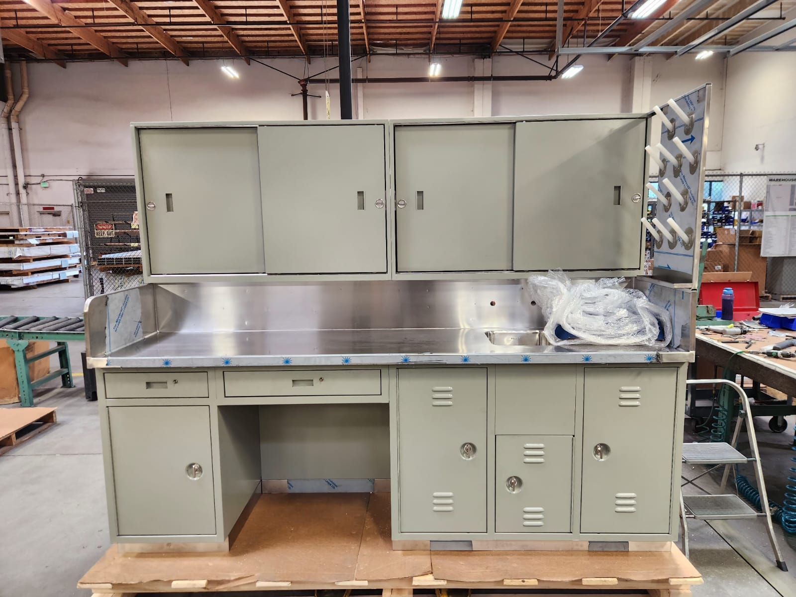 Metal workbench with cabinets and stainless steel surface. Gray and silver. Inside a factory.