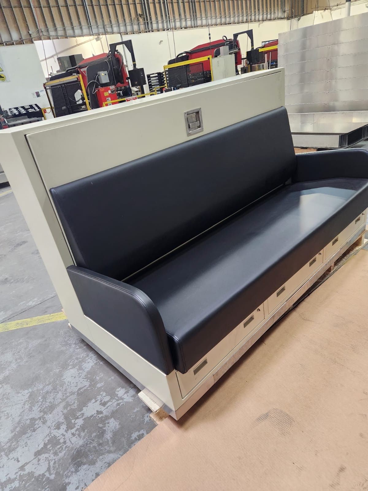 A black leather bench with a beige metal frame in a factory setting.