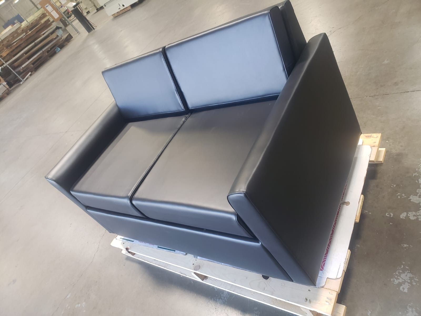 Black leather modular sofa on a wooden pallet in a warehouse.
