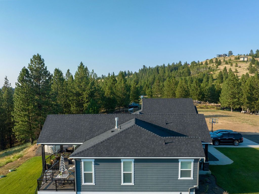 An aerial view of a house with a black roof surrounded by trees