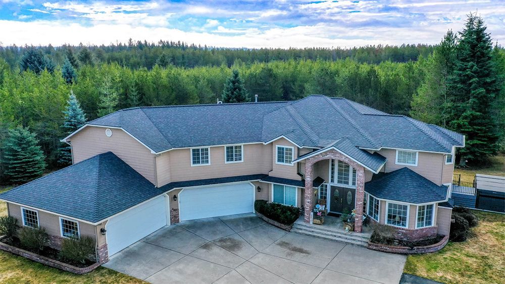 An aerial view of a large house with a blue roof surrounded by trees