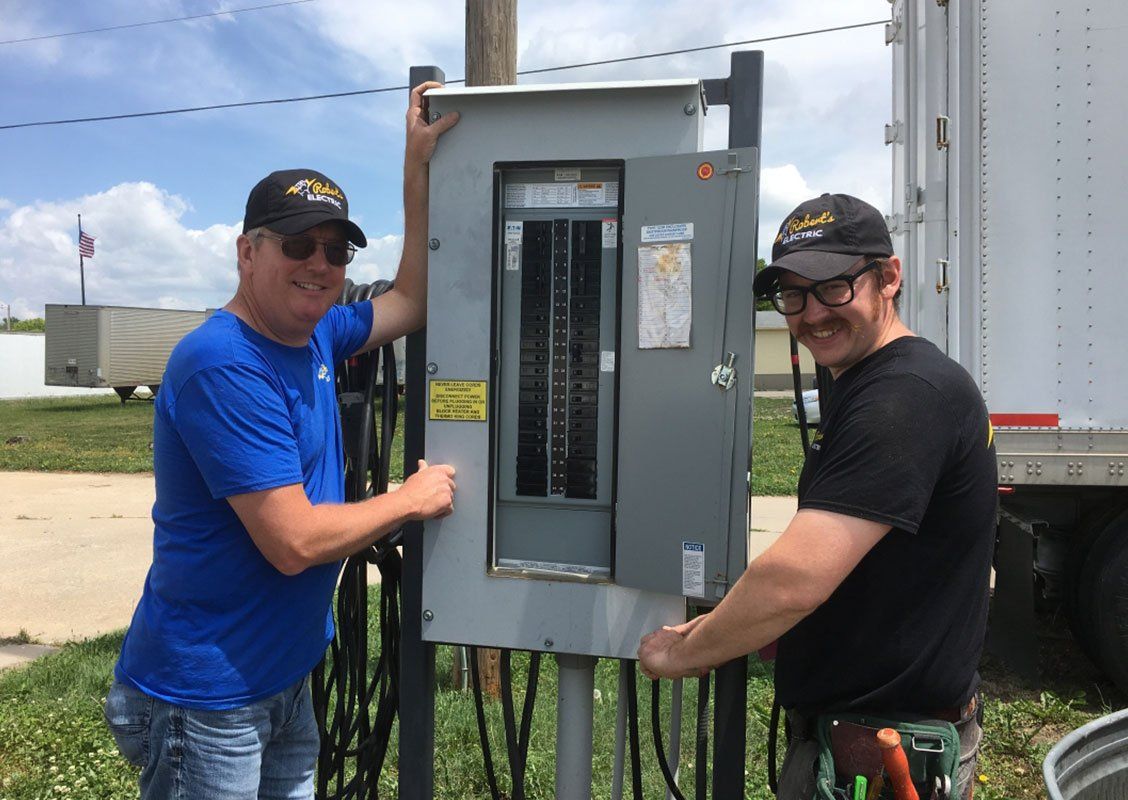 Two men smiling beside an electrical panel