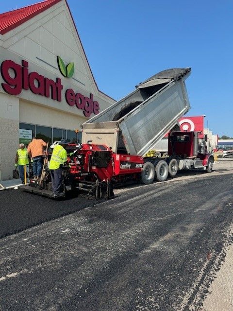 a dump truck is pouring asphalt in front of a Giant Eagle store