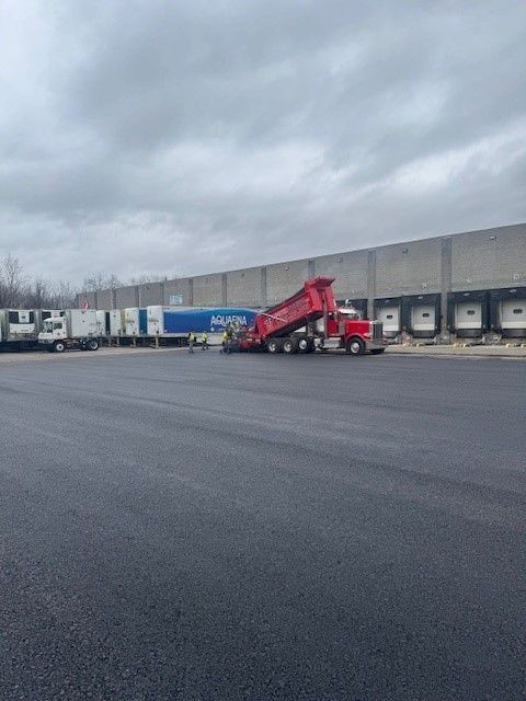 a red dump truck loaded with asphalt is parked on a commercial lot