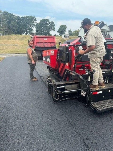 A man is standing next to a machine that is laying asphalt
