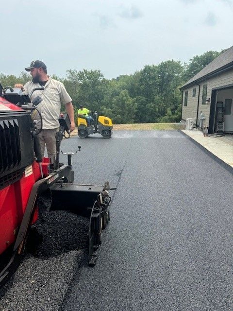 A man is standing next to a machine that is laying asphalt