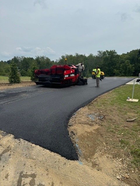 A red truck is laying asphalt on a road.