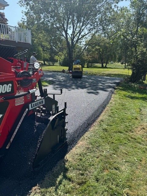 A red and black machine is laying asphalt on a driveway.