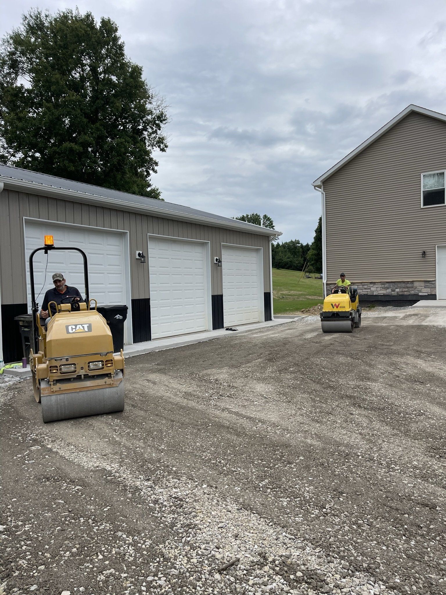 Two rollers are rolling gravel in front of a garage.