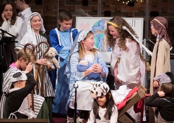 A group of children dressed in costumes are performing a nativity scene.