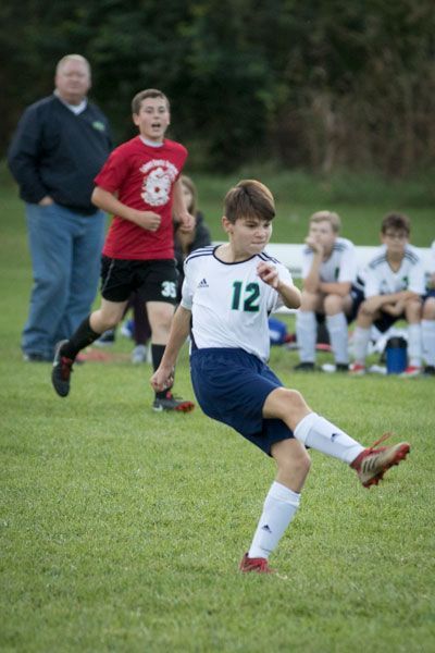 A boy wearing a number 12 jersey kicking a soccer ball