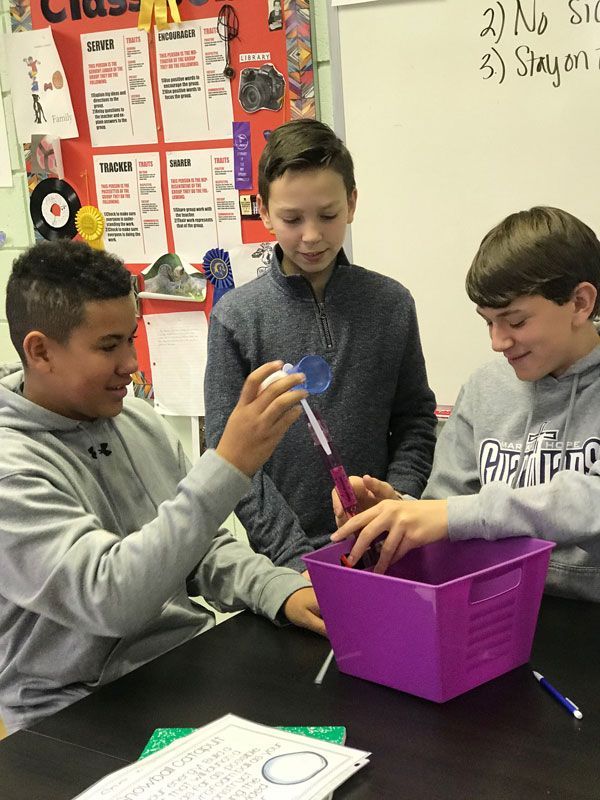 Three young boys are sitting at a table with a purple basket.