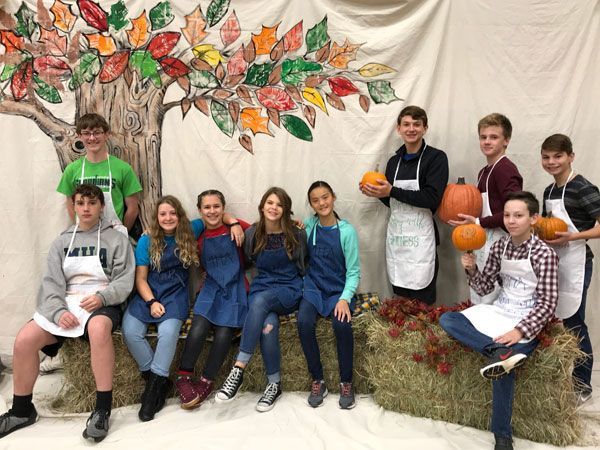 A group of young people are posing for a picture in front of a painting of a tree.