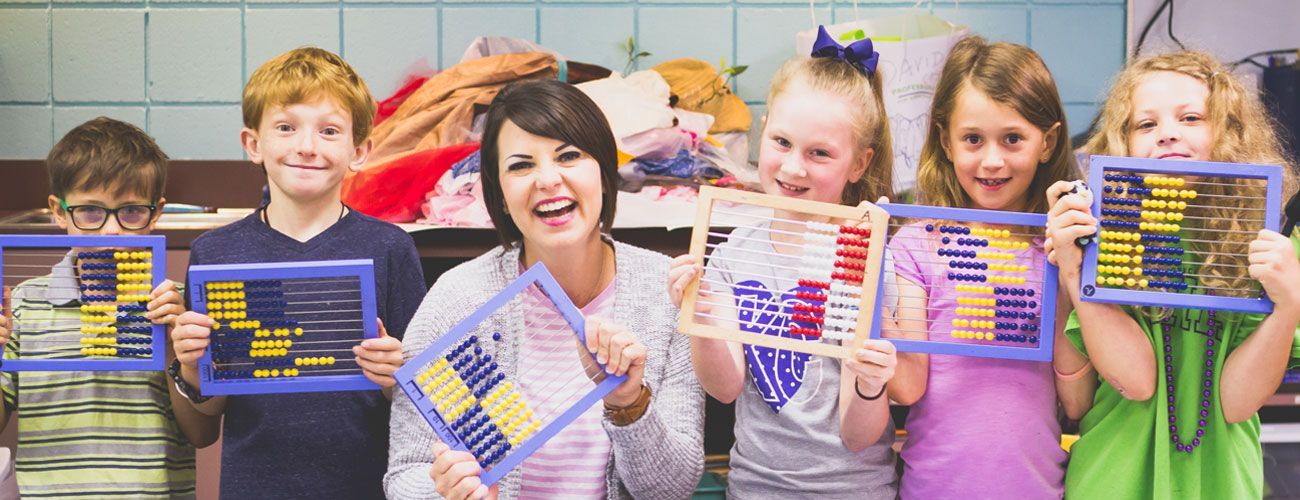 A teacher is standing next to a group of children holding abacus frames.