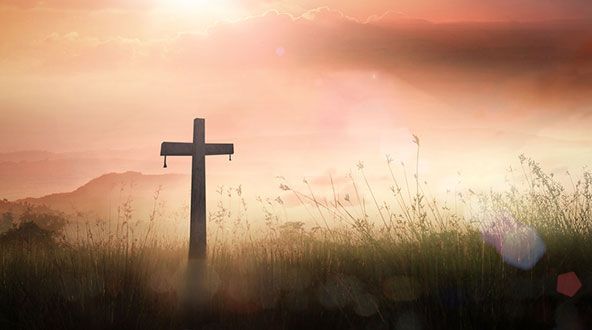 There is a cross in the middle of a field at sunset.