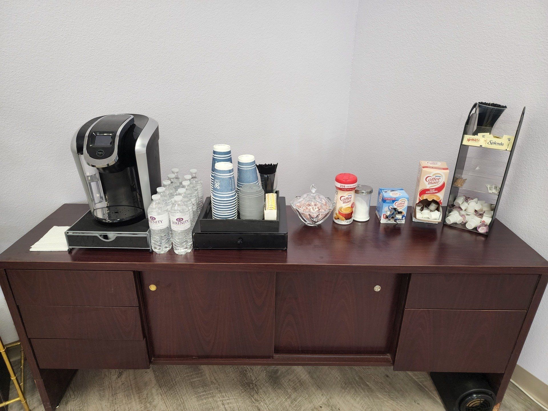 A wooden table with a coffee maker , cups , and other items on it.