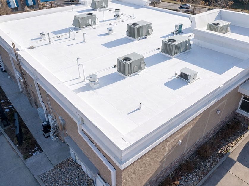 Aerial view of a flat-roofed building with white roofing and rooftop HVAC units.