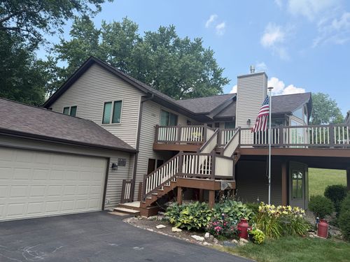 Suburban two-story house with attached garage, wooden deck, and American flag by a flower bed