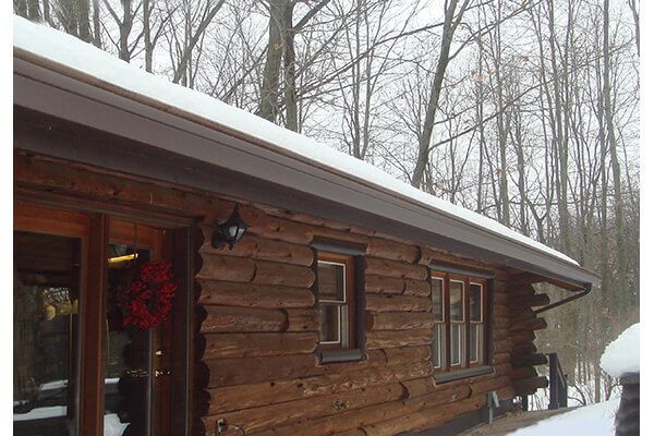 Snowy log cabin exterior with bare trees in the background